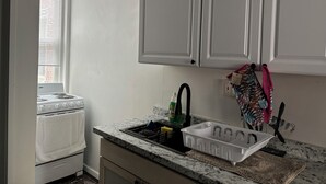 A kitchen with white cabinets, a stove, and a sink with a dish rack. - 1 bedroom apartment across from Temple Hospital (Philadelphia)