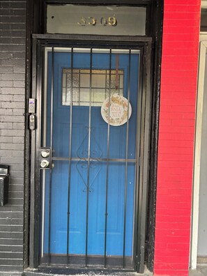 Une porte bleue avec un portail en métal, une plaque d’immatriculation et une plaque décorative portant une inscription.