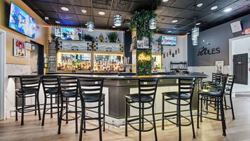 A bar area with multiple stools, a bar counter, and a television screen displaying a news program.