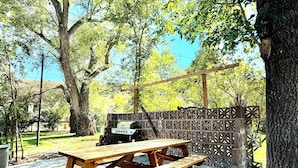 A picnic table with benches, a grill, and a decorative fence in a sunny outdoor area. - 100 year old Montana Cottage! (Manhattan)