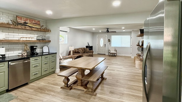 A spacious kitchen with a wooden table and benches, a stainless steel refrigerator, and a dining area with a view of the living room. - 100 year old Montana Cottage! (Manhattan)