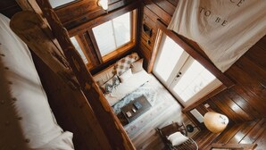 A cozy cabin-style room with a bed, a small table, and a chair. There are wooden walls and a window providing natural light.