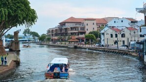 A river with a boat, buildings along the riverbank, and a bridge in the background. - All-You-Need Room for 4 Walk & Drive Around to Tourist Hotspot Eden (Melaka)