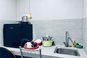 Eine Küche mit einem schwarzen Kühlschrank, einer Spüle, einem Wasserkocher, einem grünen Slow-Cooker und einer Kaffeemaschine.