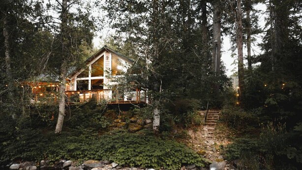 A cabin in a forest with a stream in front.