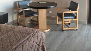 A hotel room with a bed, a round table, two chairs, and a painting on the wall.
