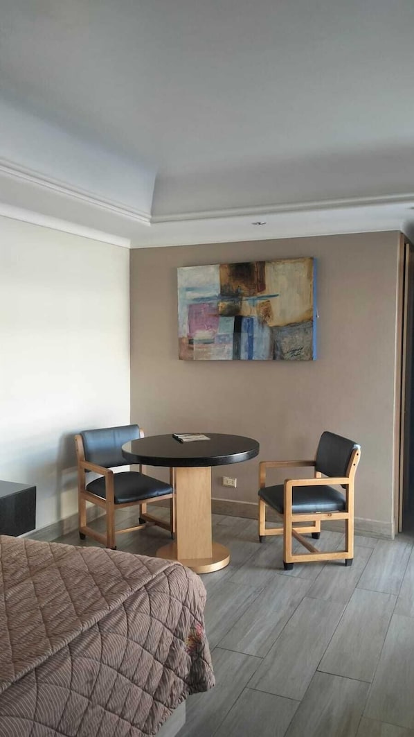 Una habitación de hotel con una cama, una mesa redonda, dos sillas y un cuadro en la pared.