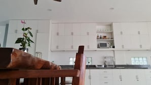 Cozinha moderna com armários brancos, ventilador de teto e área de refeições com uma cadeira de madeira.