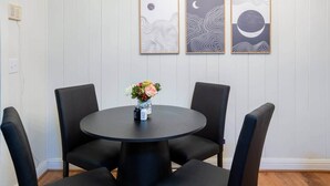 Un comedor con una mesa redonda y cuatro sillas, un florero con flores y tres cuadros en la pared.