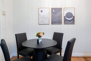 A dining area with a round table and four chairs, a vase with flowers, and three framed artworks on the wall. - Quiet Winston-Salem Retreat | Near WFU+Hospitals (Winston-Salem)