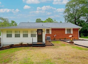 A single-story house with a front porch, a brick section, and a small garden area. - Southern Comfort  Near WFU, Hospitals & Top Spots (Winston-Salem)