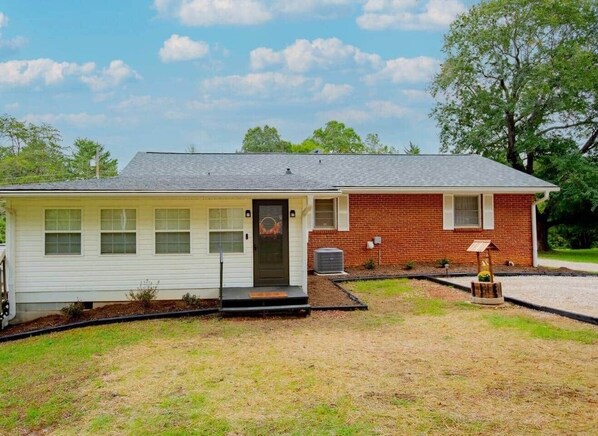 A single-story house with a front porch, a brick section, and a small garden area. - Charming Retreat Near WFU, Hospitals, & Top Spots (Winston-Salem)