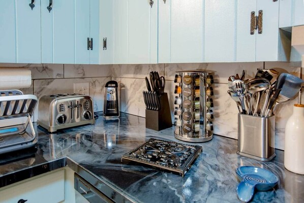 A kitchen with light blue cabinets, a marble countertop, a toaster, a kettle, a spice rack, and various utensils.