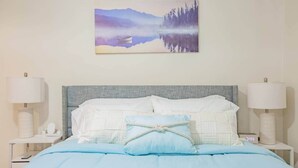 Ein Schlafzimmer mit einem Bett, zwei Nachttischen, einem Beistelltisch, einem Gemälde von einer Berglandschaft und einer Uhr.