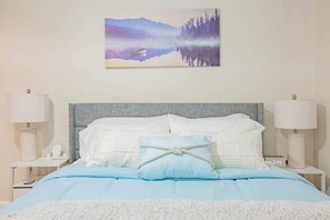 A bedroom with a bed, two bedside tables, a nightstand, a painting of a mountain landscape, and a clock.