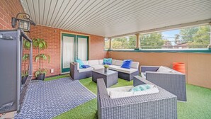 En overdækket terrasse med fletmøbler, en murstensvæg og udsigt til kvarteret.