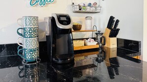 Kaffestation med kaffemaskine, kopper og et sæt knive på en bordplade.