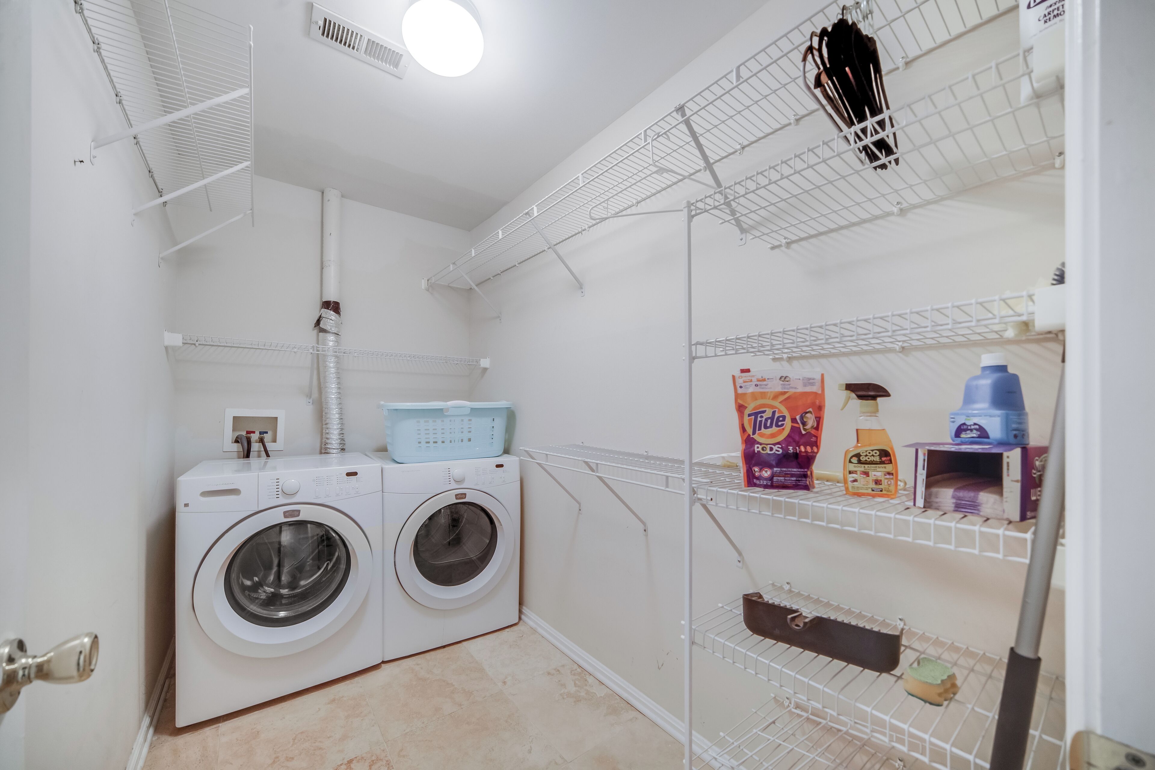 Une buanderie équipée d’un lave-linge à chargement frontal, d’étagères contenant des produits de nettoyage et d’un étendoir.