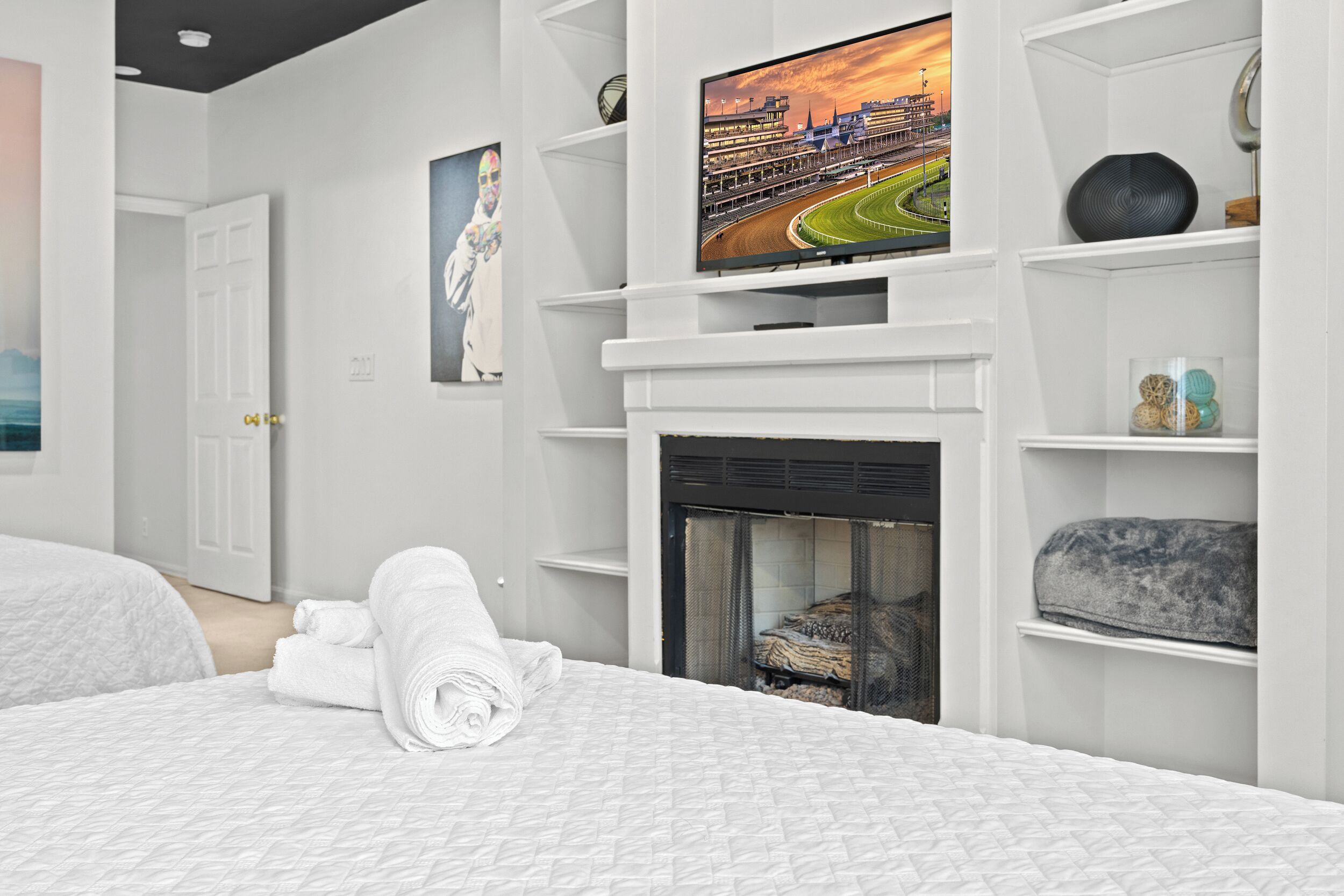 Un dormitorio moderno con chimenea, un televisor montado encima y toallas dobladas con cuidado sobre la cama.