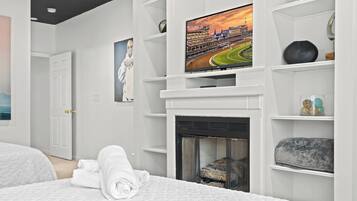 Un dormitorio moderno con chimenea, un televisor montado encima y toallas dobladas con cuidado sobre la cama.