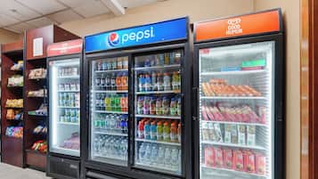 A row of beverage vending machines with a Pepsi logo, surrounded by shelves stocked with snacks and other food items.