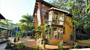 A two-story wooden house with large windows, surrounded by lush greenery and a wooden deck. - The Dock Resort  (Roatan)