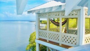 A white wooden structure with a hammock and a view of the sea. - The Dock Resort  (Roatan)