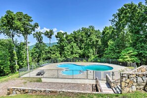 Une piscine bordée de pierres et dotée d’une terrasse en bois, entourée d’une clôture et d’arbres.