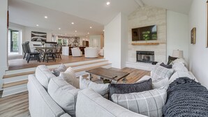 Een ruime woonkamer met een moderne open haard, een eethoek en een keuken op de achtergrond.