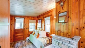 Un dormitorio de cabaña de madera con chimenea de piedra, una cama con almohadas y una ventana con persianas.