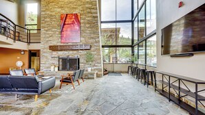 Eine geräumige Lobby mit Steinboden, Kamin, großem Fenster und einer Sitzecke mit Sofa und Sesseln.