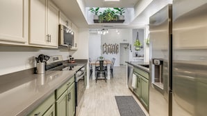Cozinha moderna com eletrodomésticos de aço inoxidável, área de jantar com mesa de madeira e um claraboia.