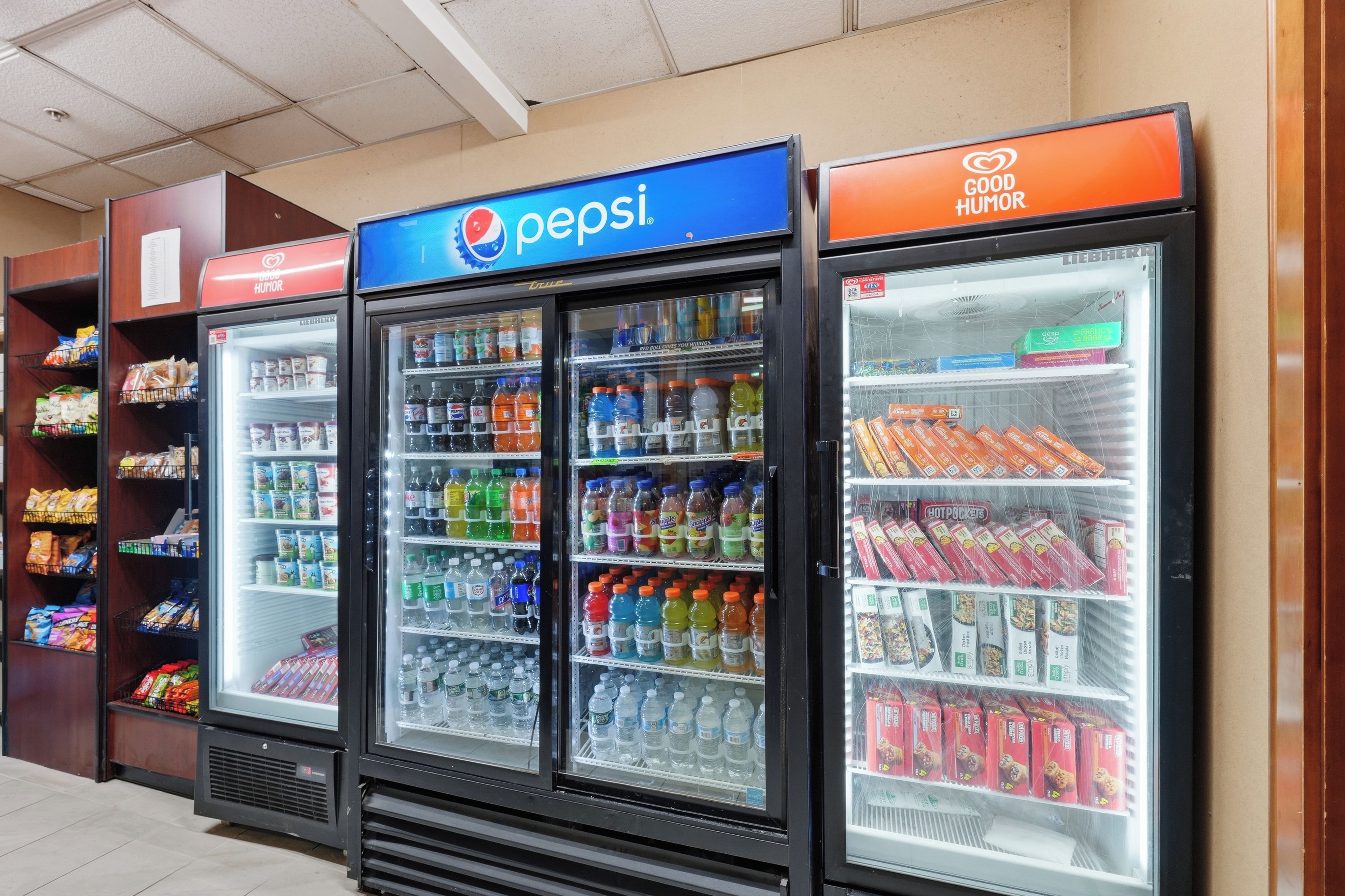 Une rangée de distributeurs automatiques de boissons arborant le logo Pepsi, entourés d’étagères remplies d’en-cas et d’autres produits alimentaires.
