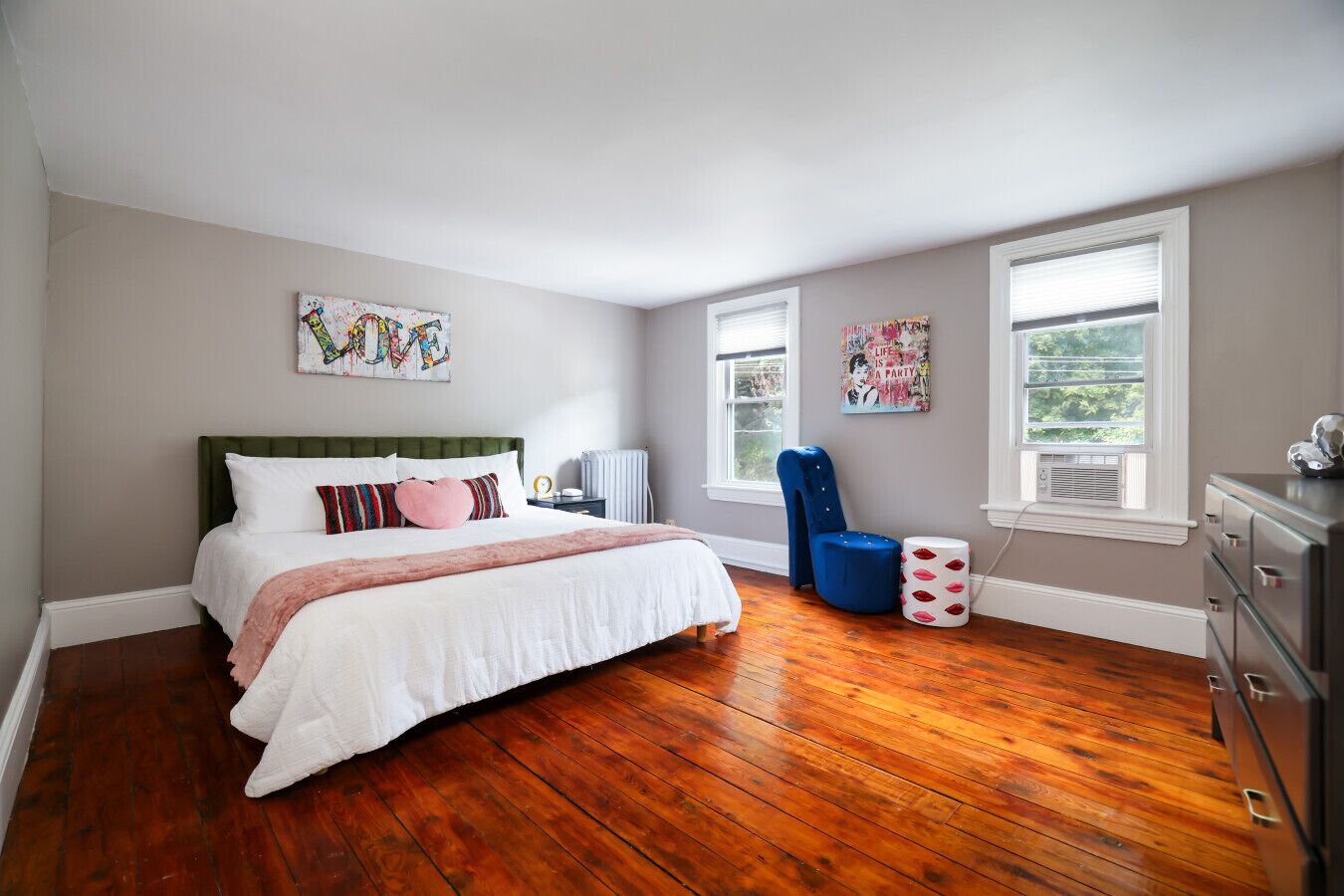 Un dormitorio con cama, una silla, cómoda y obras de arte en las paredes.