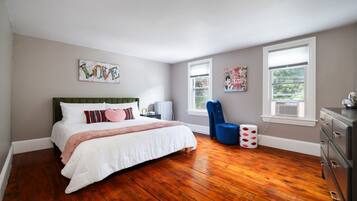 Un dormitorio con cama, una silla, cómoda y obras de arte en las paredes.