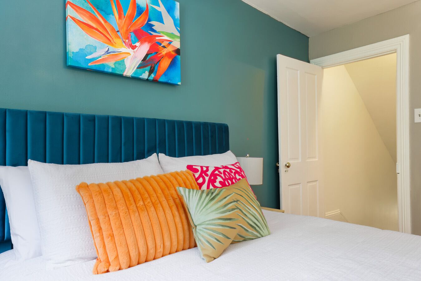 Quarto com cabeceira verde-azulado, roupa de cama branca e almofadas coloridas.