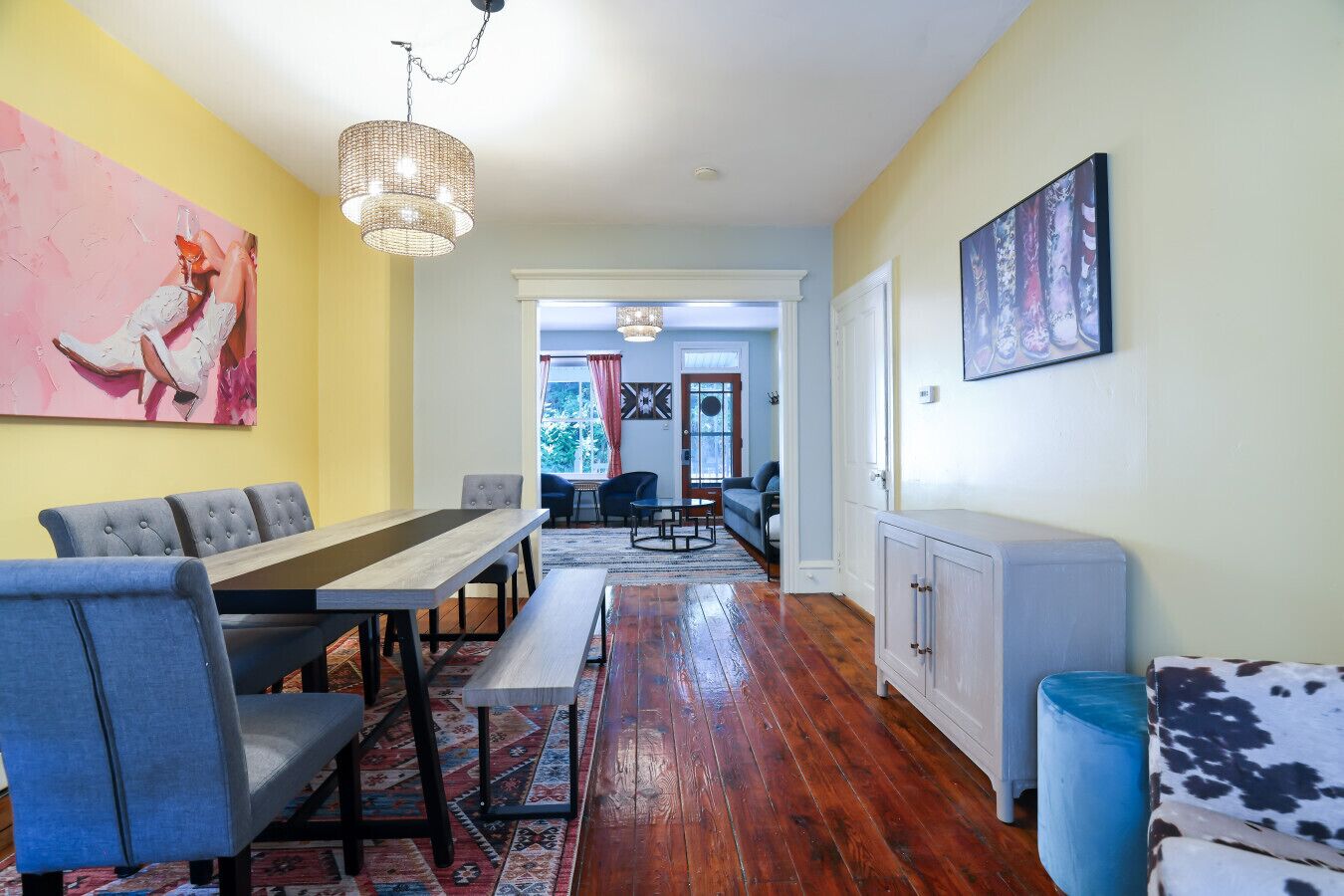 A dining area with a long table, chairs, and a patterned rug. There is a blue sofa and a cabinet in the background.