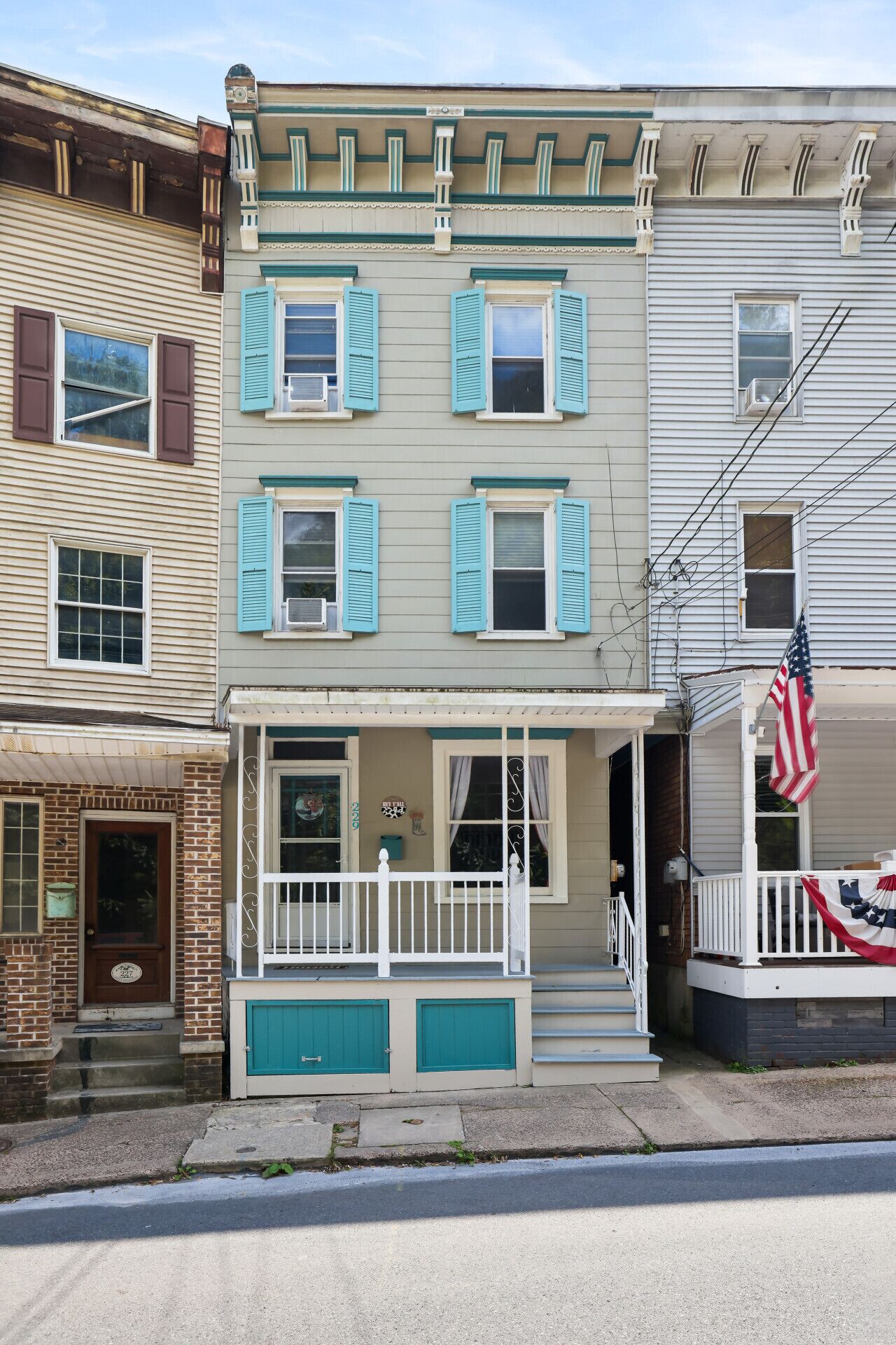 A two-story building with a porch, a brick entrance, and a flag.