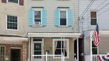 A two-story building with a porch, a brick entrance, and a flag.