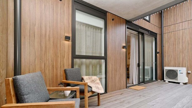 Ein moderner Außenbereich mit zwei Holzstühlen und einem Tisch, einem großen Fenster und einer Klimaanlage.
