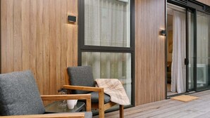 Ein moderner Außenbereich zum Sitzen mit Holzmöbeln und einer Glastür zu einem Raum.