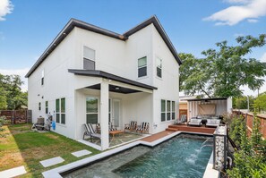 Una casa de dos pisos con piscina, mobiliario exterior y patio cercado.