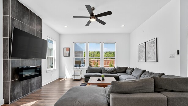 A modern living room with a sectional sofa, a flat-screen TV, and a ceiling fan. - The Hugo | Sleeps 10 (Dallas)