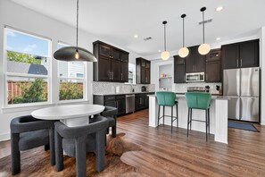 A modern kitchen with dark cabinets, a stainless steel refrigerator, and a dining area with a round table and chairs.