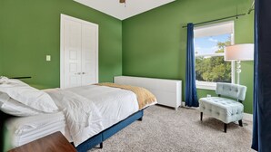 A bedroom with a bed, a chair, a window with curtains, a radiator, and a ceiling fan. - The Hugo | Sleeps 10 (Dallas)