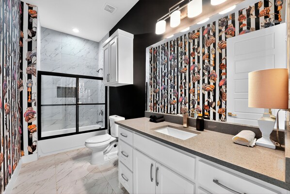 A modern bathroom with a glass shower enclosure, a large mirror with a seafood print backsplash, and a white sink.