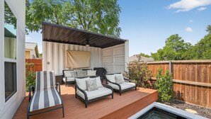 A covered outdoor seating area with two lounge chairs and two sofas, a small pool, and a wooden deck. - The Hugo | Sleeps 10 (Dallas)