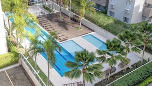 A rooftop pool area with lounge chairs and palm trees. - Apto c Piscina e Quadras no Recreio (Rio de Janeiro)