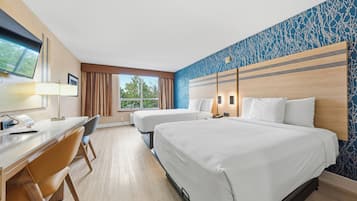 Habitació d'hotel amb dos llits, una taula, una cadira, un televisor i una finestra amb cortines.