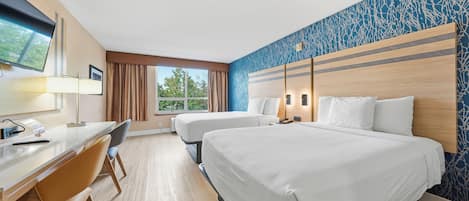Ein Hotelzimmer mit zwei Betten, einem Schreibtisch, einem Stuhl, einem Fernseher und einem Fenster mit Vorhängen.